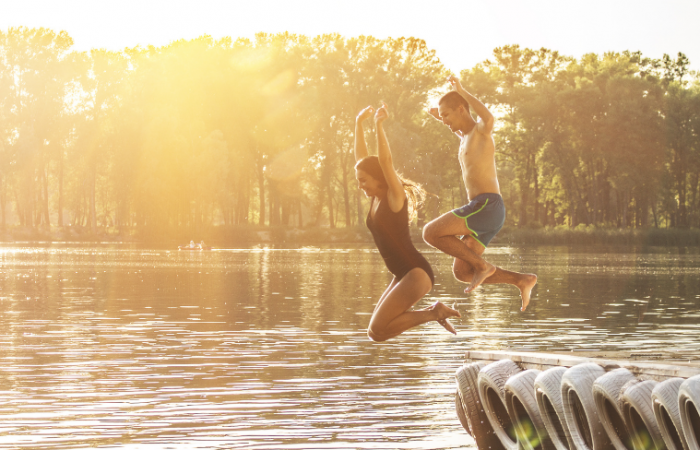 a young couple jumping into a lake in the summer